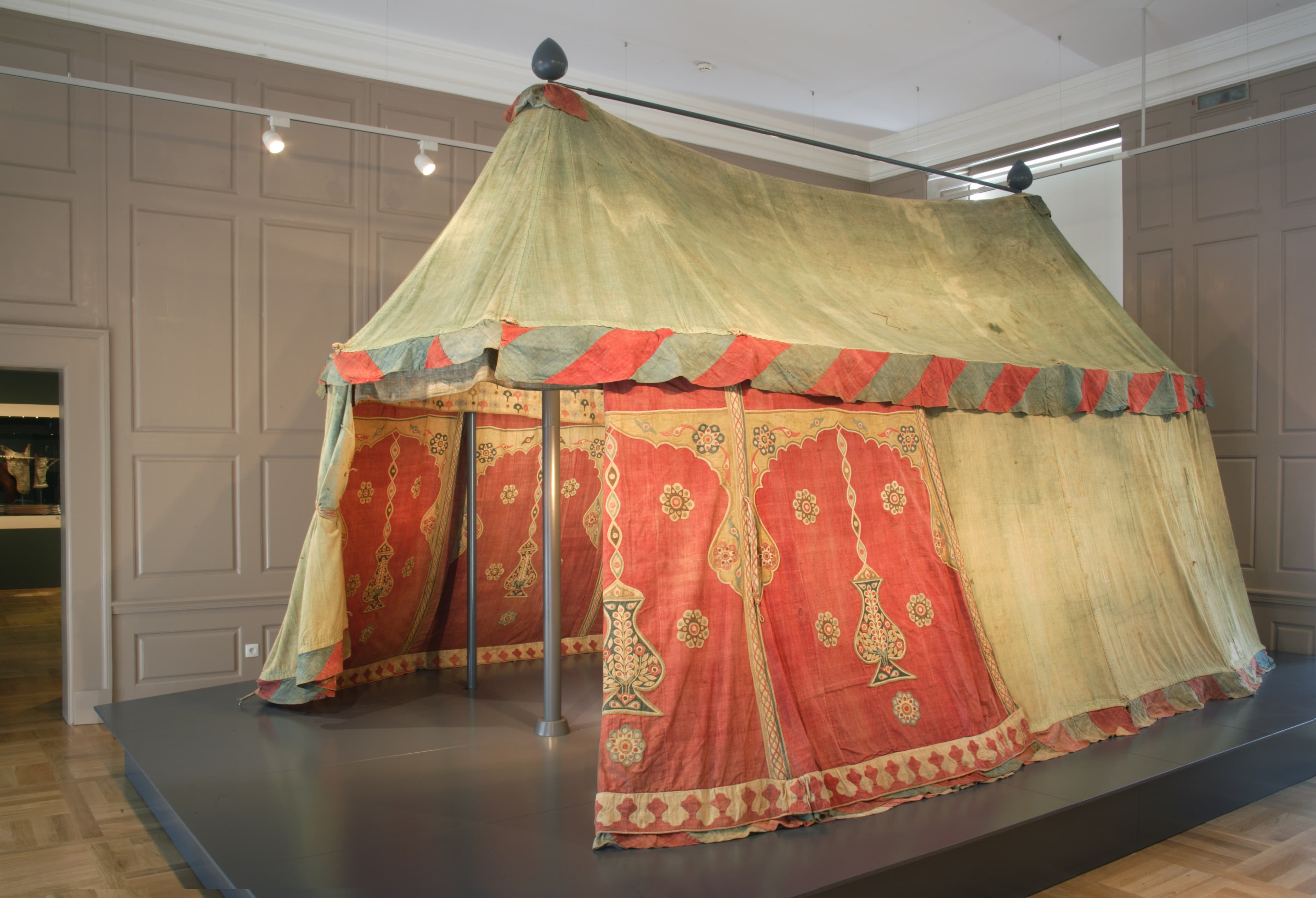 Ein historisches Zelt mit kunstvollen roten und goldenen Mustern, ausgestellt in einem Museum.
