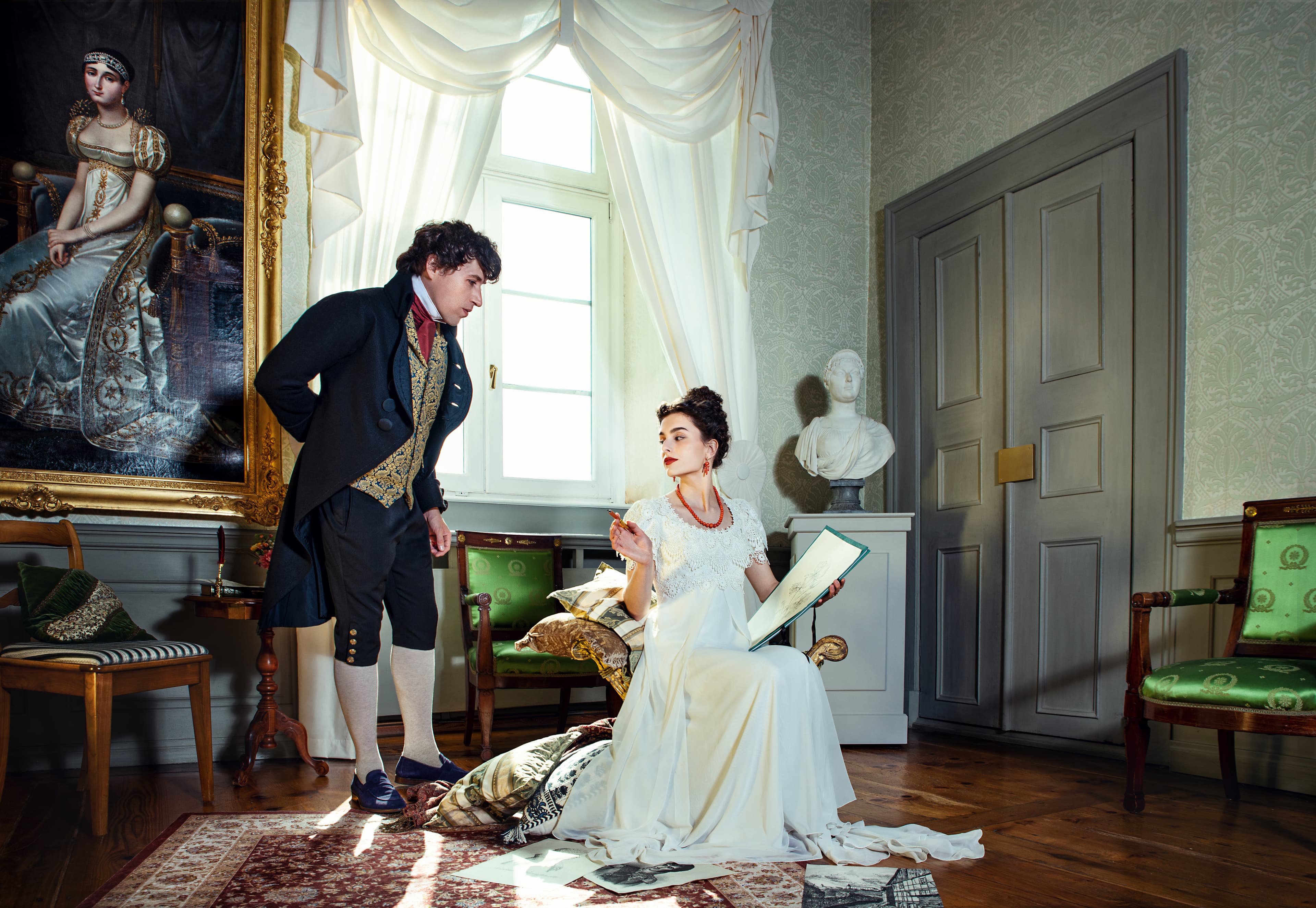 Ein Mann in zeitgenössischer Kleidung steht neben einer sitzenden Frau in einem weißen Kleid, die ein Buch hält, in einem eleganten Raum mit einem großen Gemälde und einer Büste.