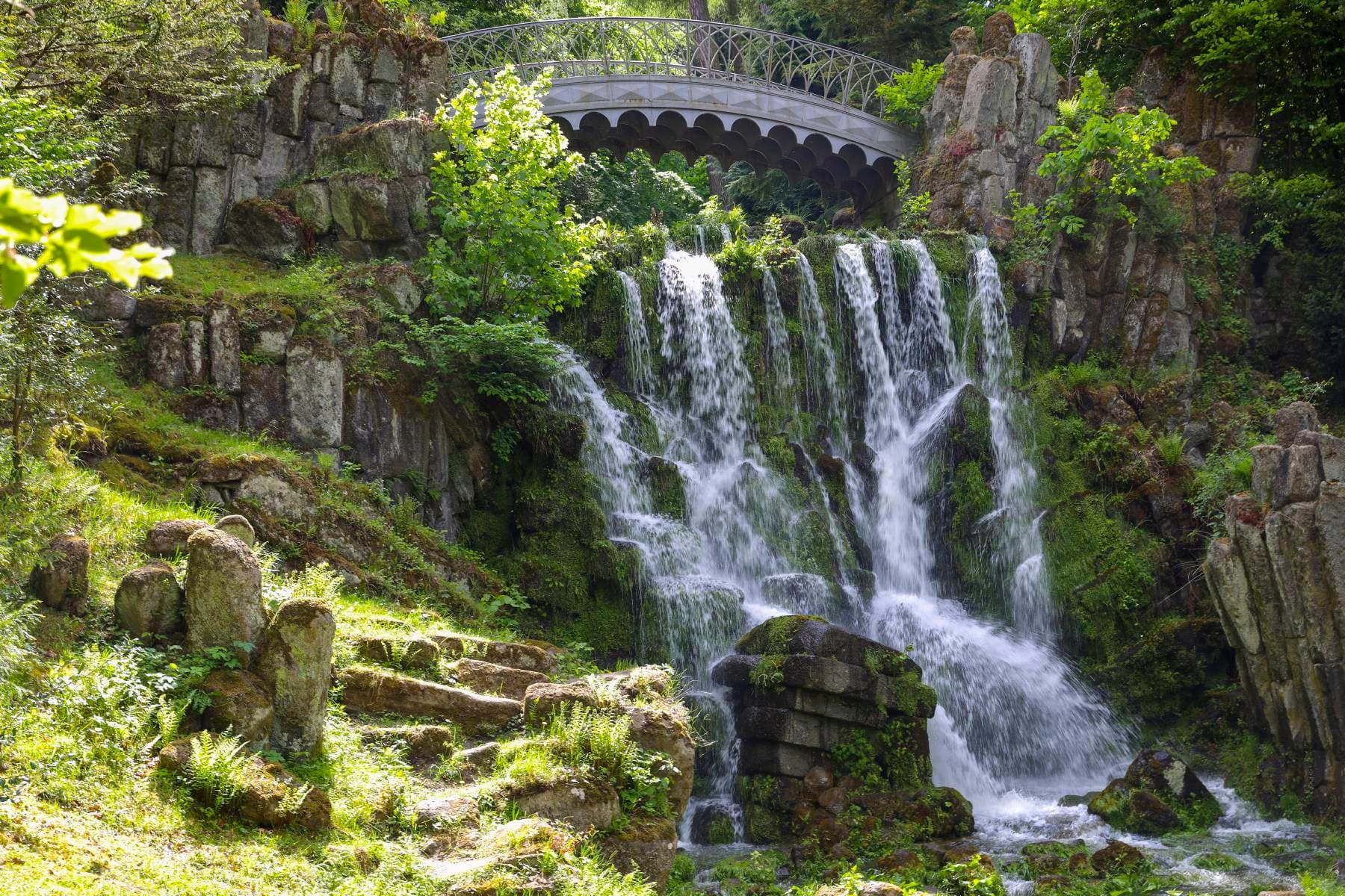 Waterfall with bridge running over it, embedded in the green Bergpark