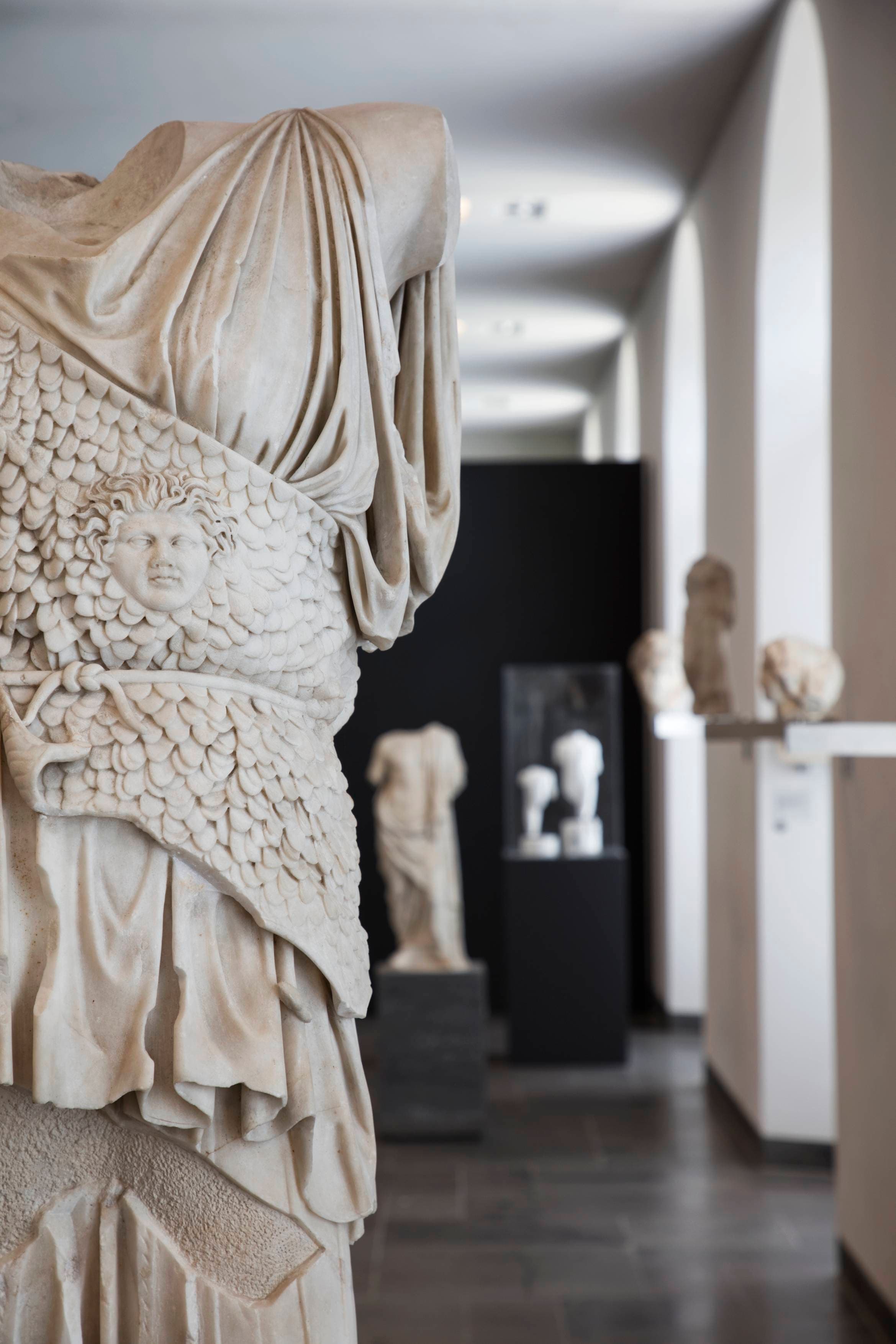 Marmorstatue eines Torsos mit aufwendiger Rüstung in einer Museumsgalerie, umgeben von anderen ausgestellten klassischen Skulpturen.