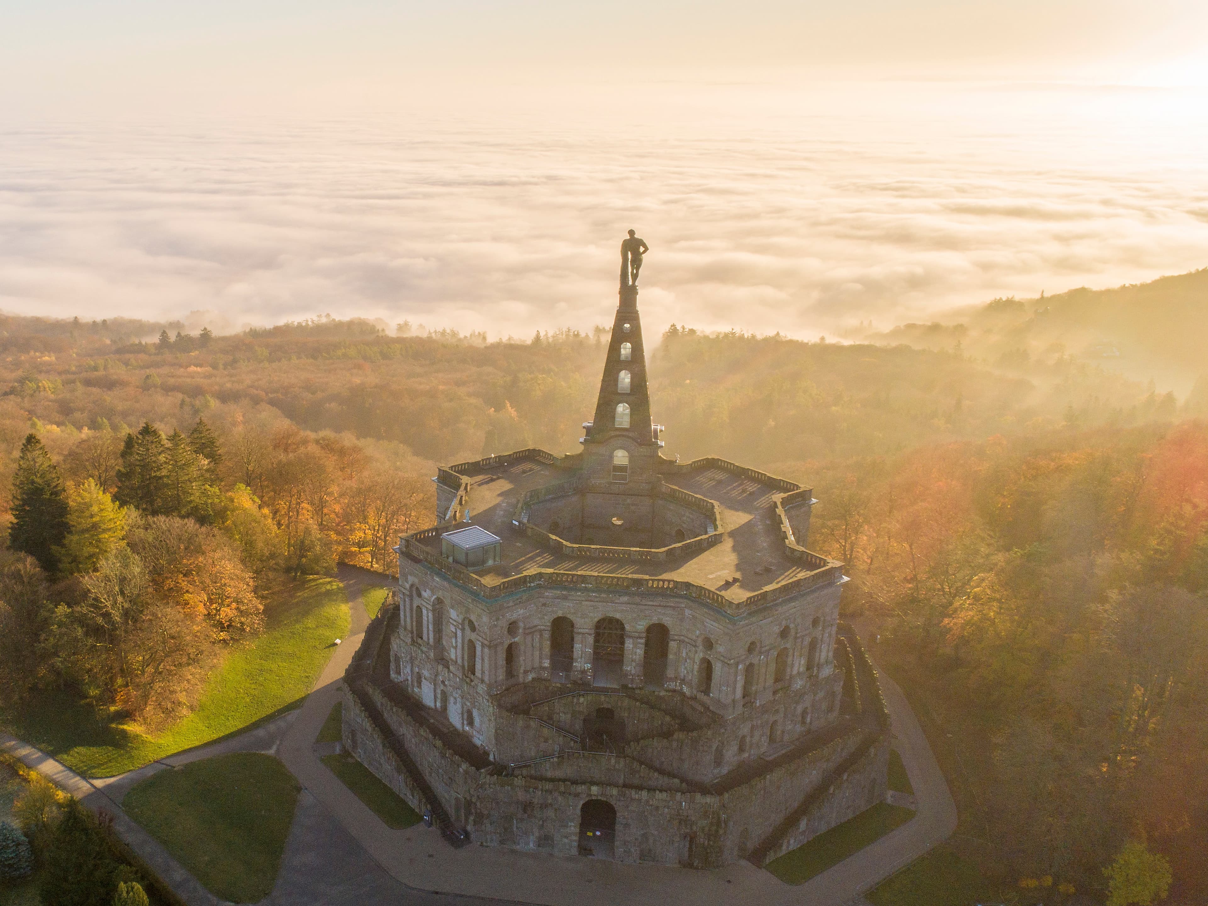 Aerial view of the Hercules monument in Kassel, Germany, surrounded by autumn trees and a misty landscape at sunrise.